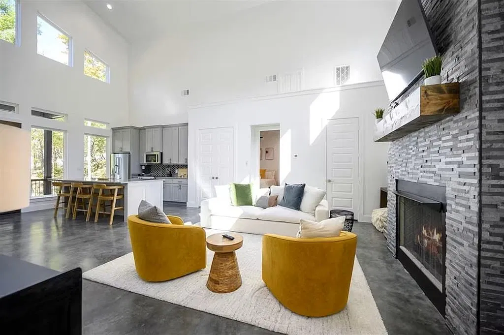 Great room with stone fireplace, yellow swivel chairs and a tall ceiling